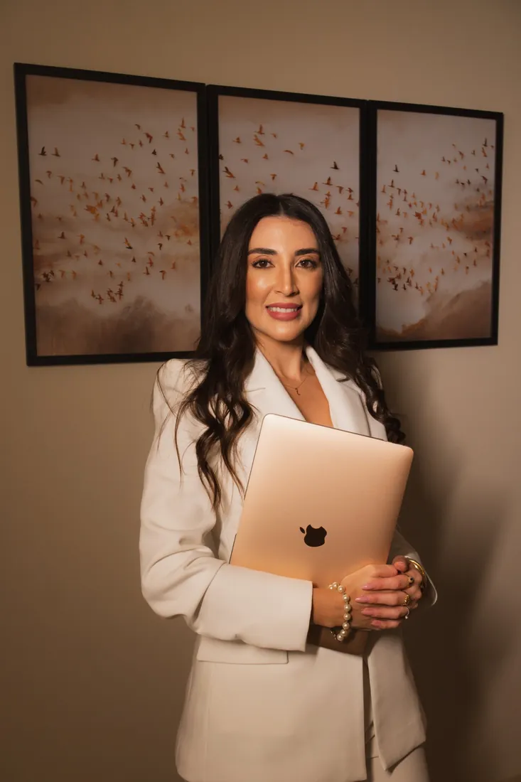 Jennifer de terno branco segurando um notebook diante do tríptico de pássaros em voo
